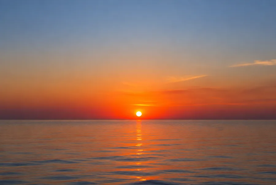 Orange and red sunset sky over calm sea with the sun just above the horizon